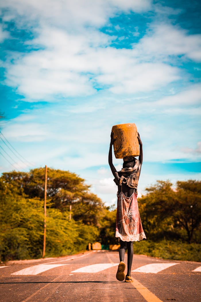 A young girl carries a container while walking on a road in Turkana, Kenya during sunset.
